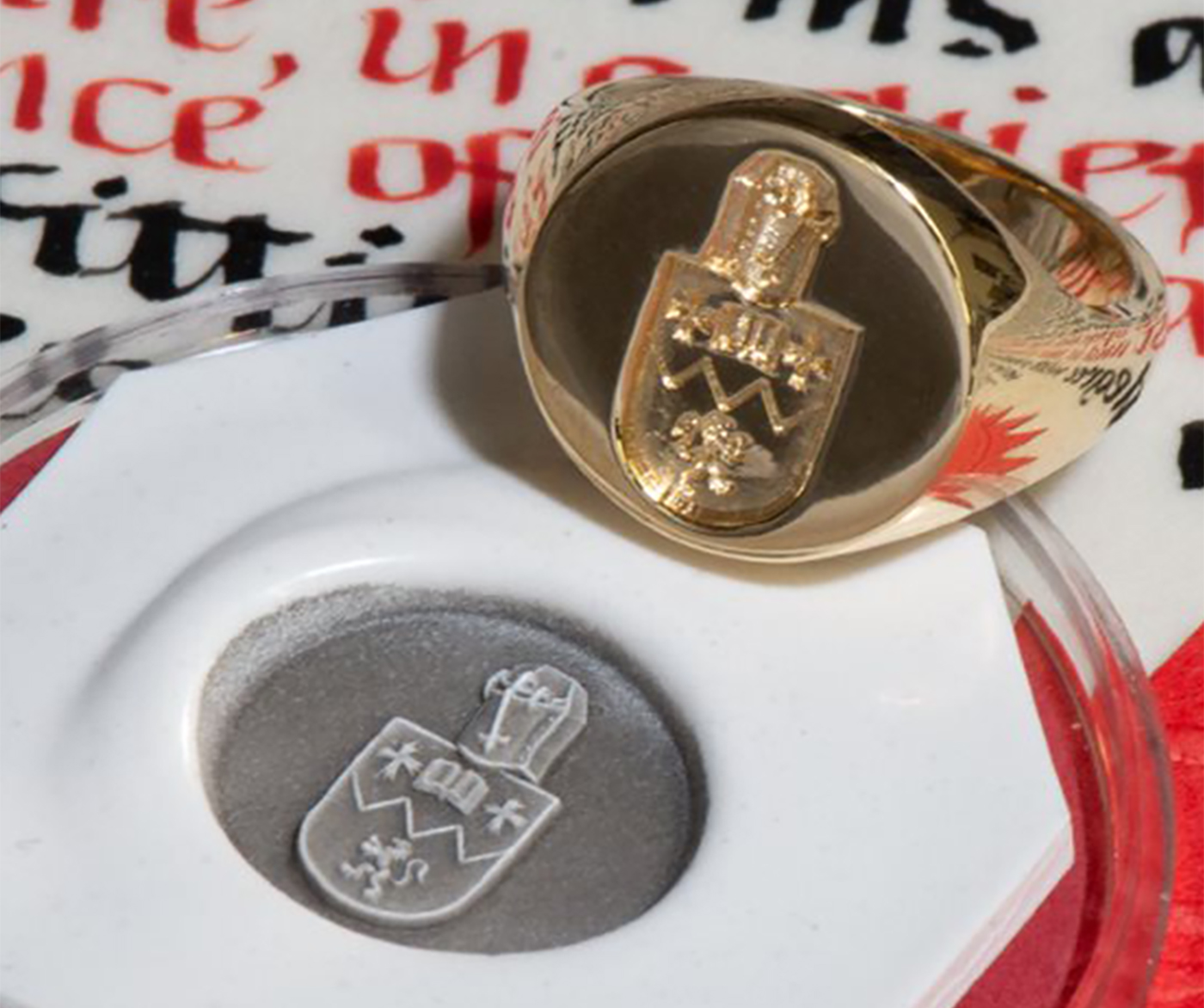 Gold signet ring with coat of arms engraving with seal on medieval calligraphy script background