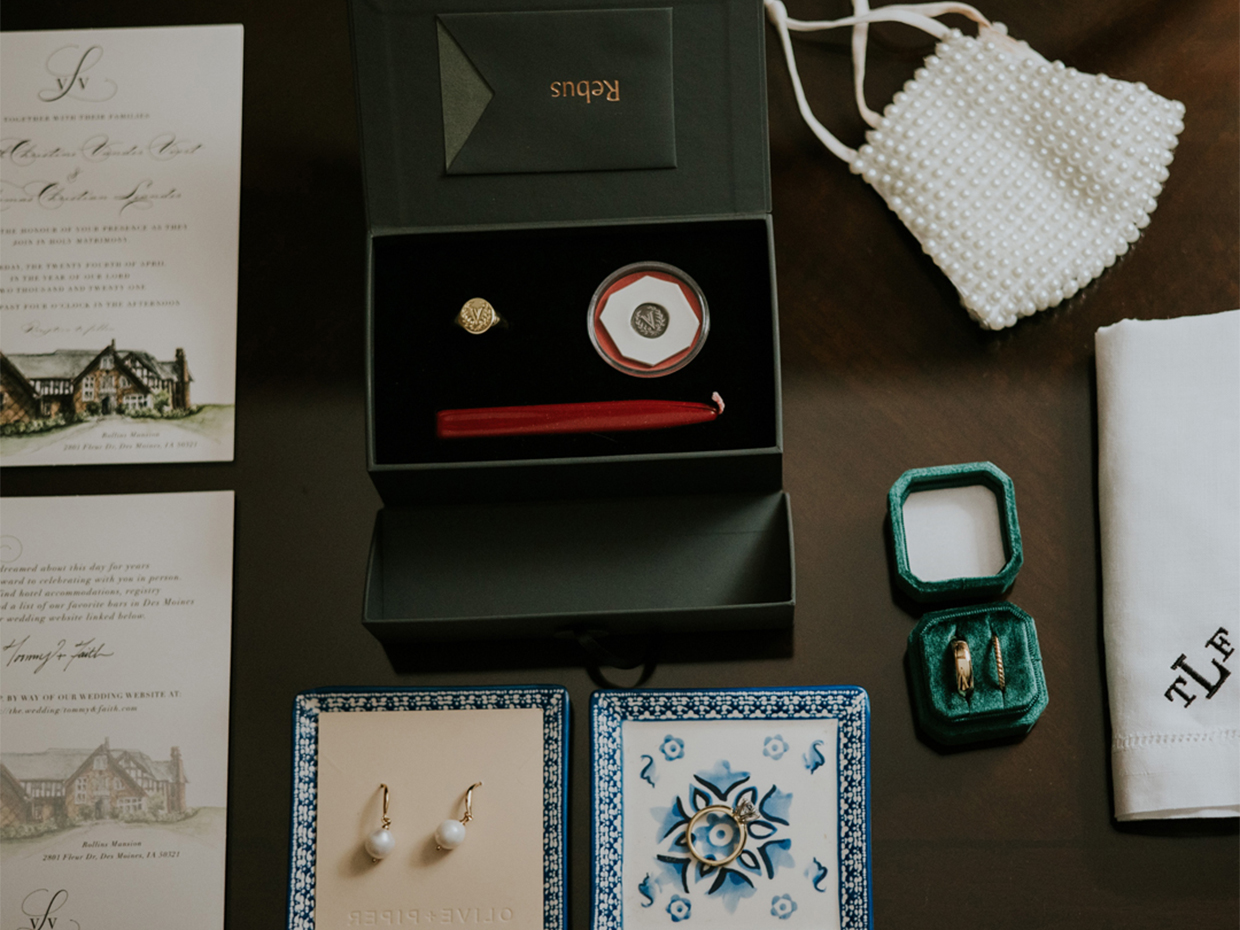 Aerial photograph of wedding paraphernalia including pearl earrings, gold signet ring, embroidered handkerchief, and wedding invitation 