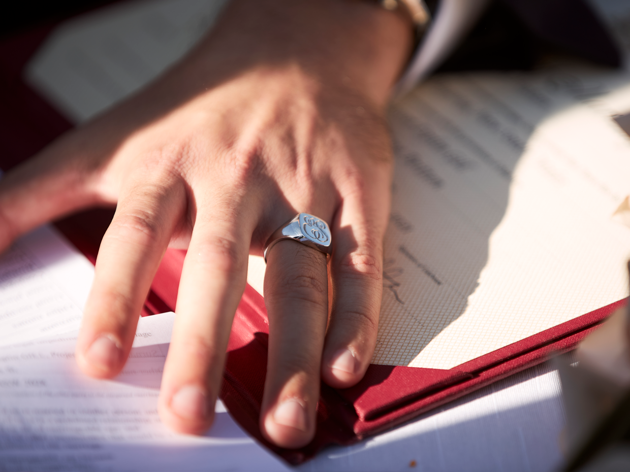 Hand of groom on wedding day wearing bespoke engraved signet ring on his ring finger.